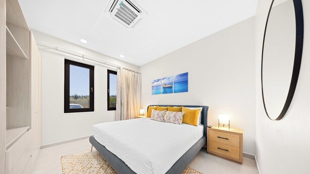 A bedroom with a bed, a nightstand, a window, and a wall-mounted mirror. - Walk to Beach: 4BR Oasis w/ Pool, Spa, View (Noord)