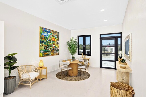 A modern interior with a round dining table, chairs, a large painting, and a view through a glass door.