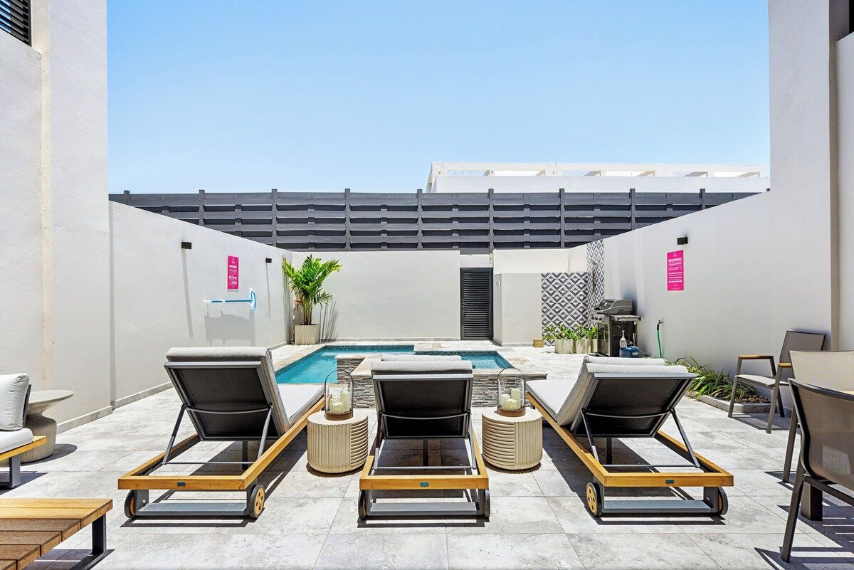 Un espace piscine aménagé sur le toit, avec des chaises longues, une piscine et une pergola au-dessus.