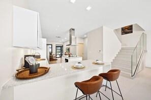 A modern kitchen with a central island, bar stools, and a staircase leading to an upper level.