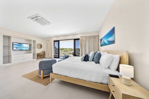 Ein modernes Schlafzimmer mit einem großen Bett, einem Fernseher, einem Schreibtisch und Blick aus dem Fenster.