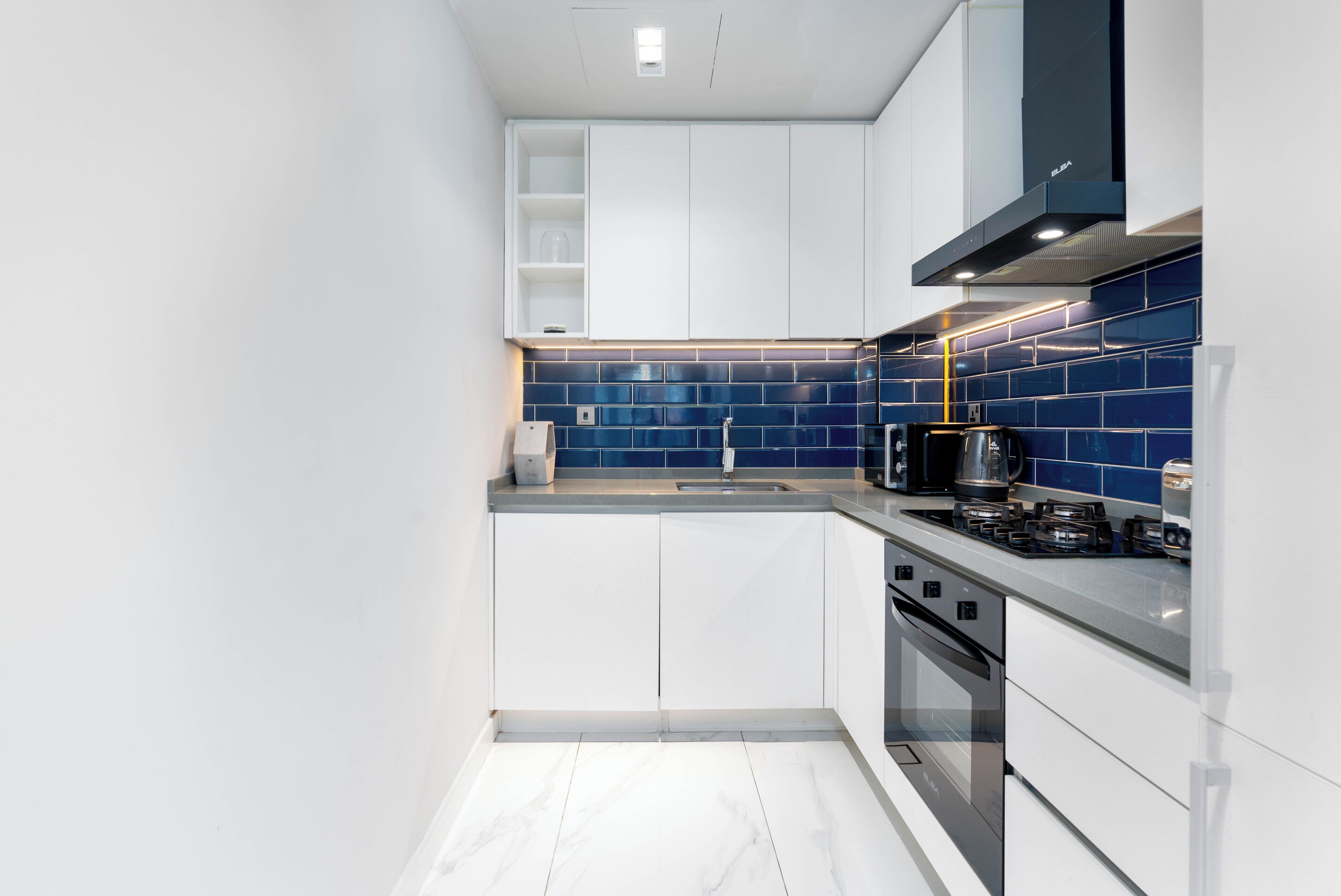 A modern kitchen with white cabinets, a blue tiled backsplash, a stainless steel stove, and a built-in oven.