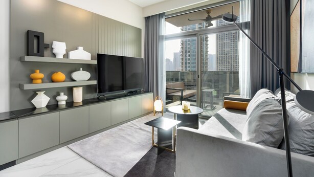 Un salon moderne avec un canapé, un téléviseur, une petite table et un balcon offrant une vue sur la ville.