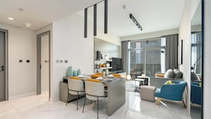 A modern living room with a sofa, a dining area with chairs and a table, and a kitchen with cabinets and a TV.