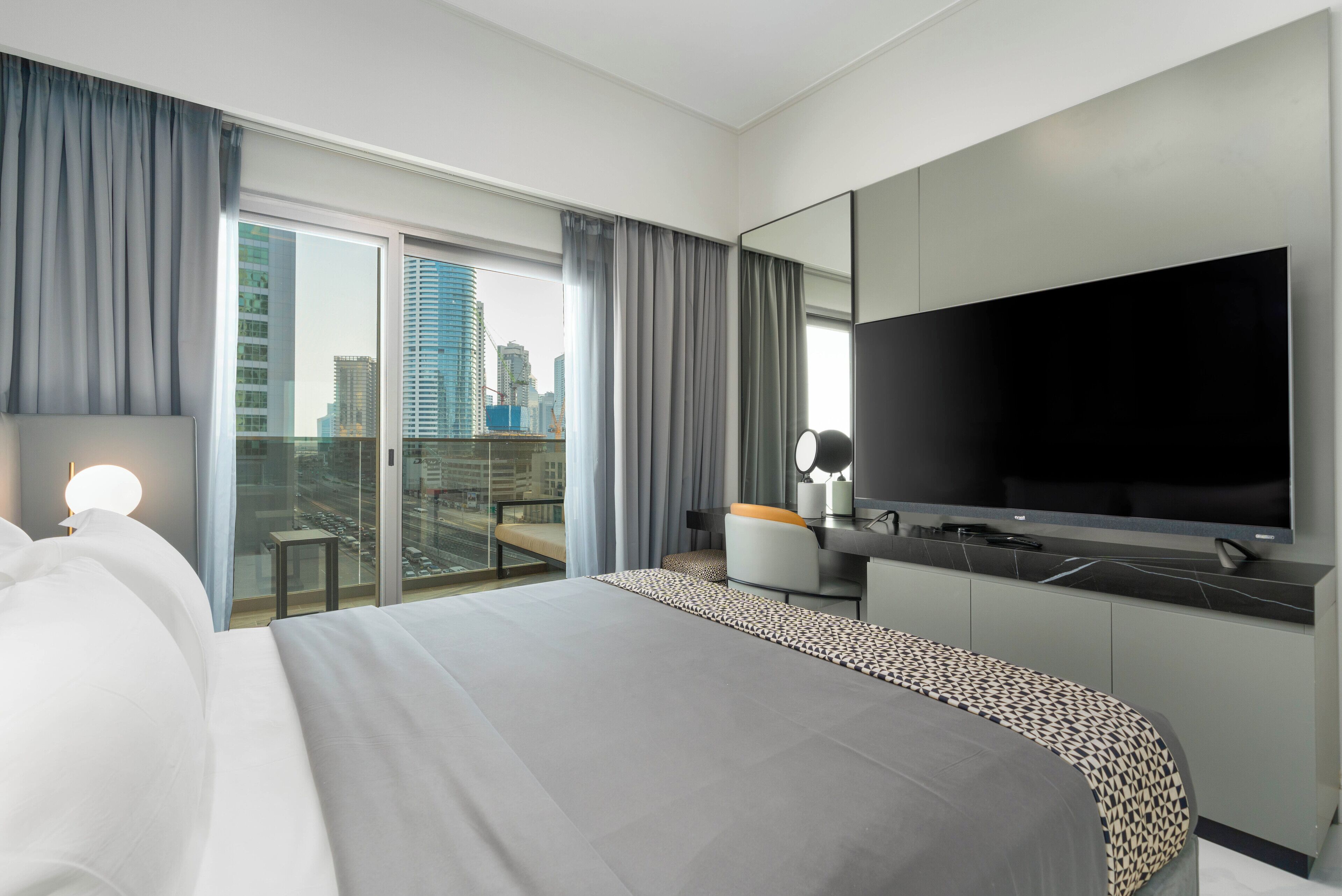 Een moderne hotelkamer met een groot bed, een flatscreen televisie, een bureau en een balkon met uitzicht over de stad.