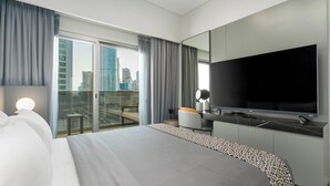 A modern hotel room with a large bed, a flat-screen TV, a desk, and a balcony with a city view.