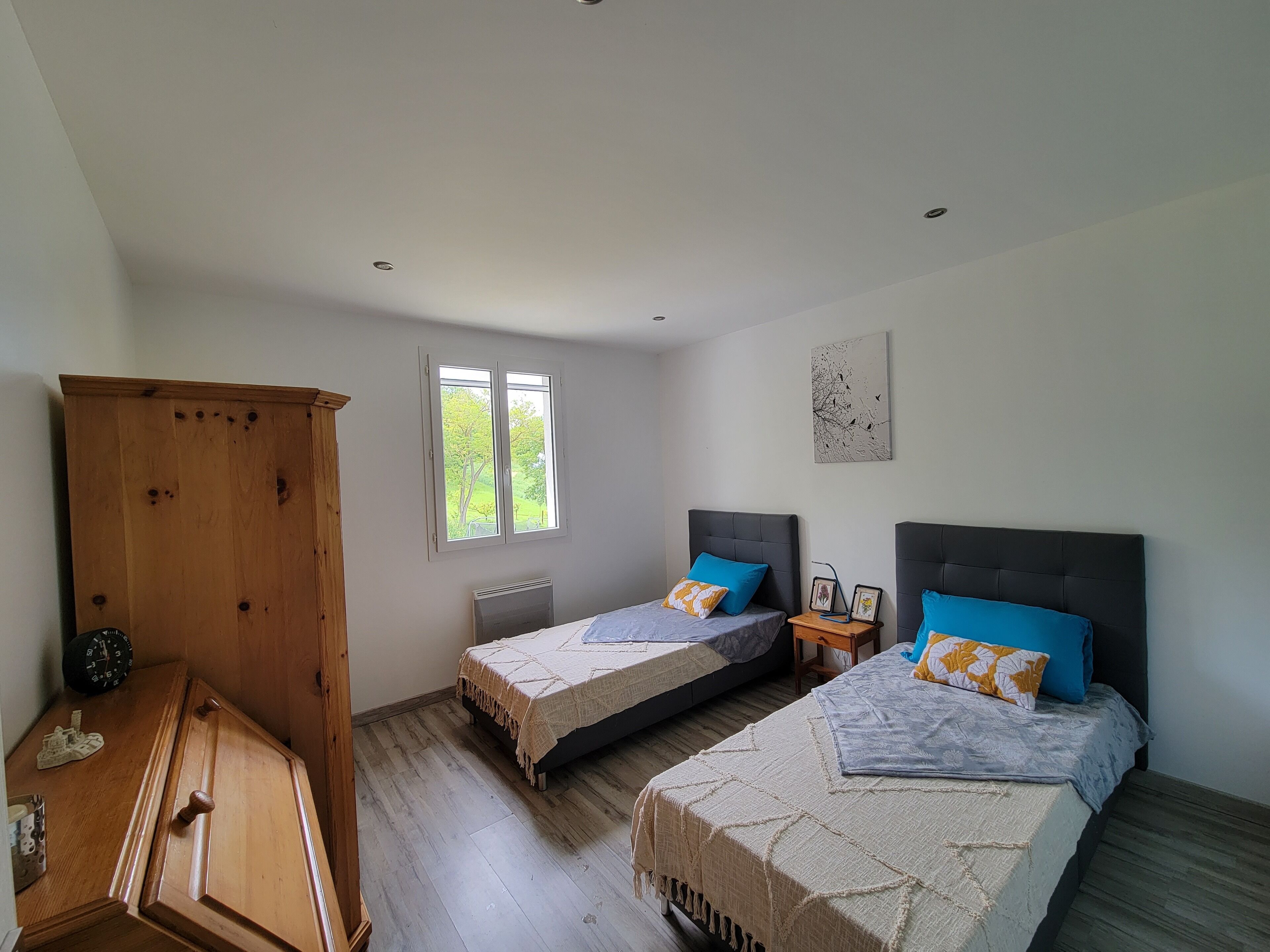 Een slaapkamer met twee bedden, een houten kledingkast, een raam en een aan de muur hangend schilderij.