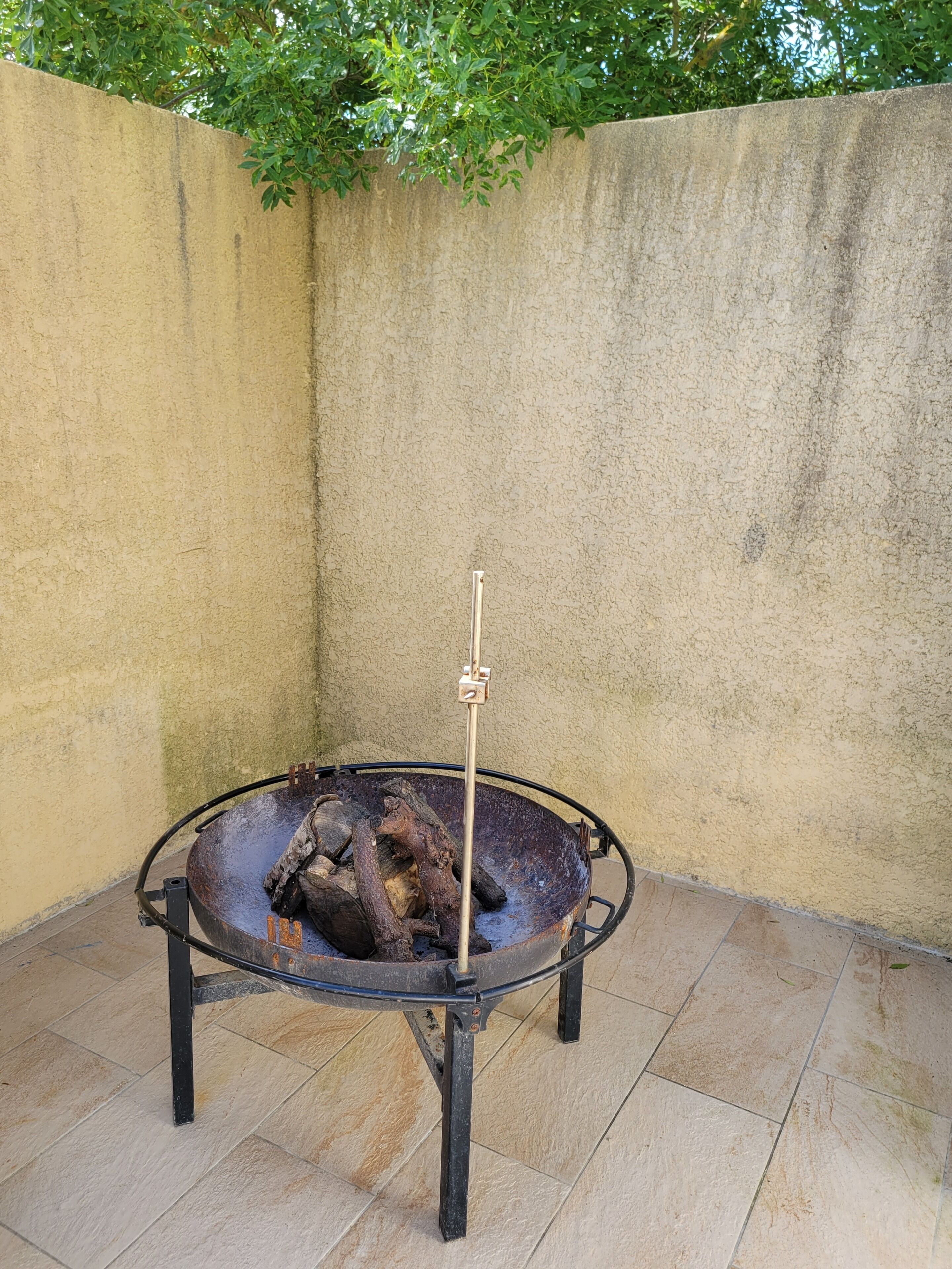 Una parrilla redonda para exteriores con un soporte de metal, rodeada por un patio con baldosas.