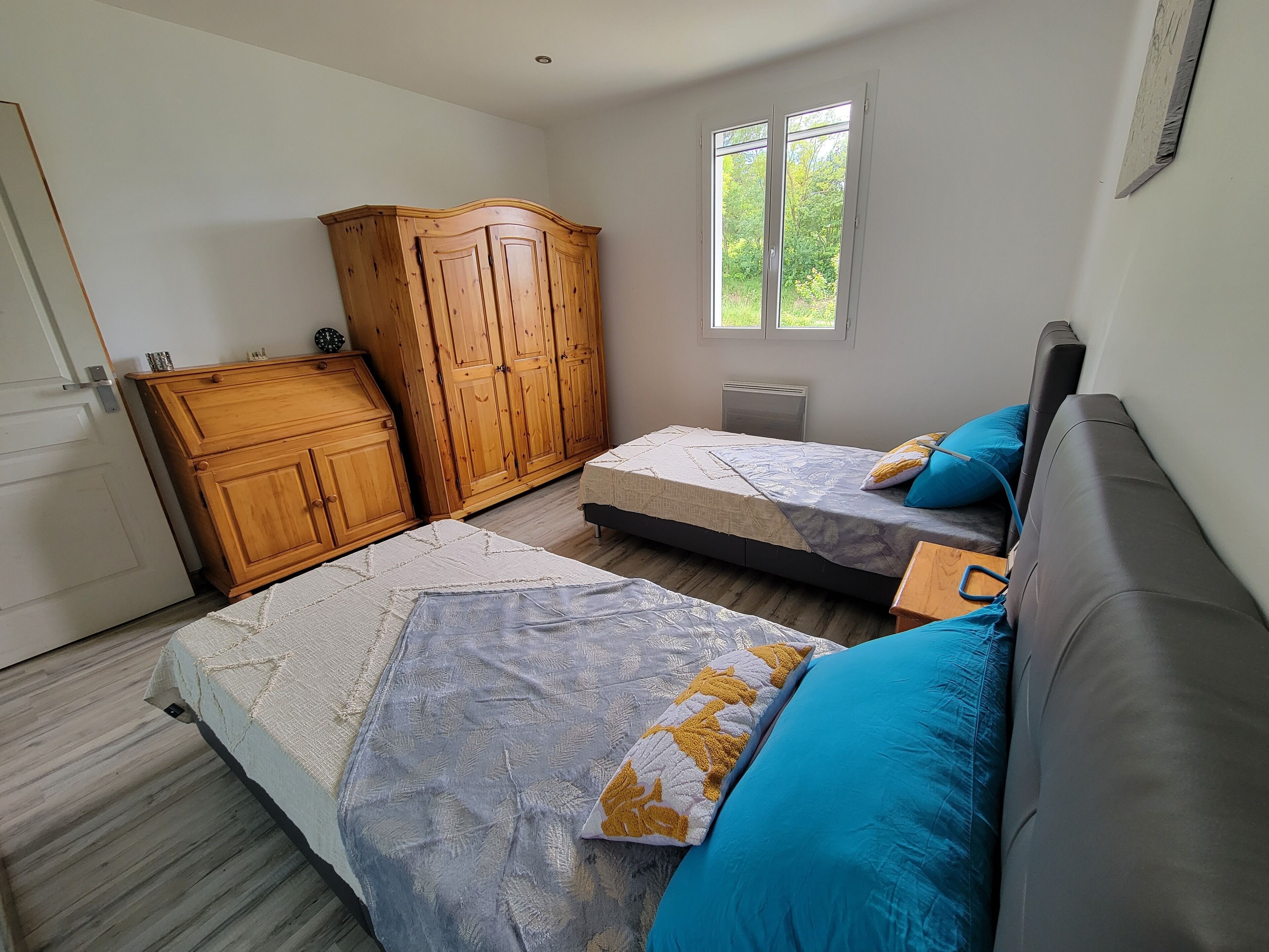 A bedroom with two beds, wooden wardrobe, and a window with a view of greenery.