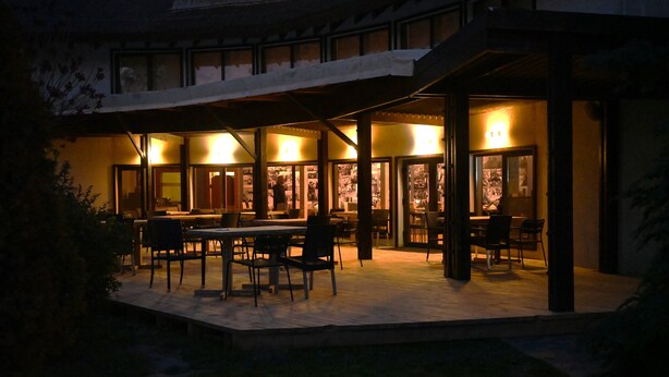 An outdoor dining area with tables and chairs, illuminated by warm lighting, and a covered walkway leading to a building entrance. - Egreta By Hoxton (Murighiol)