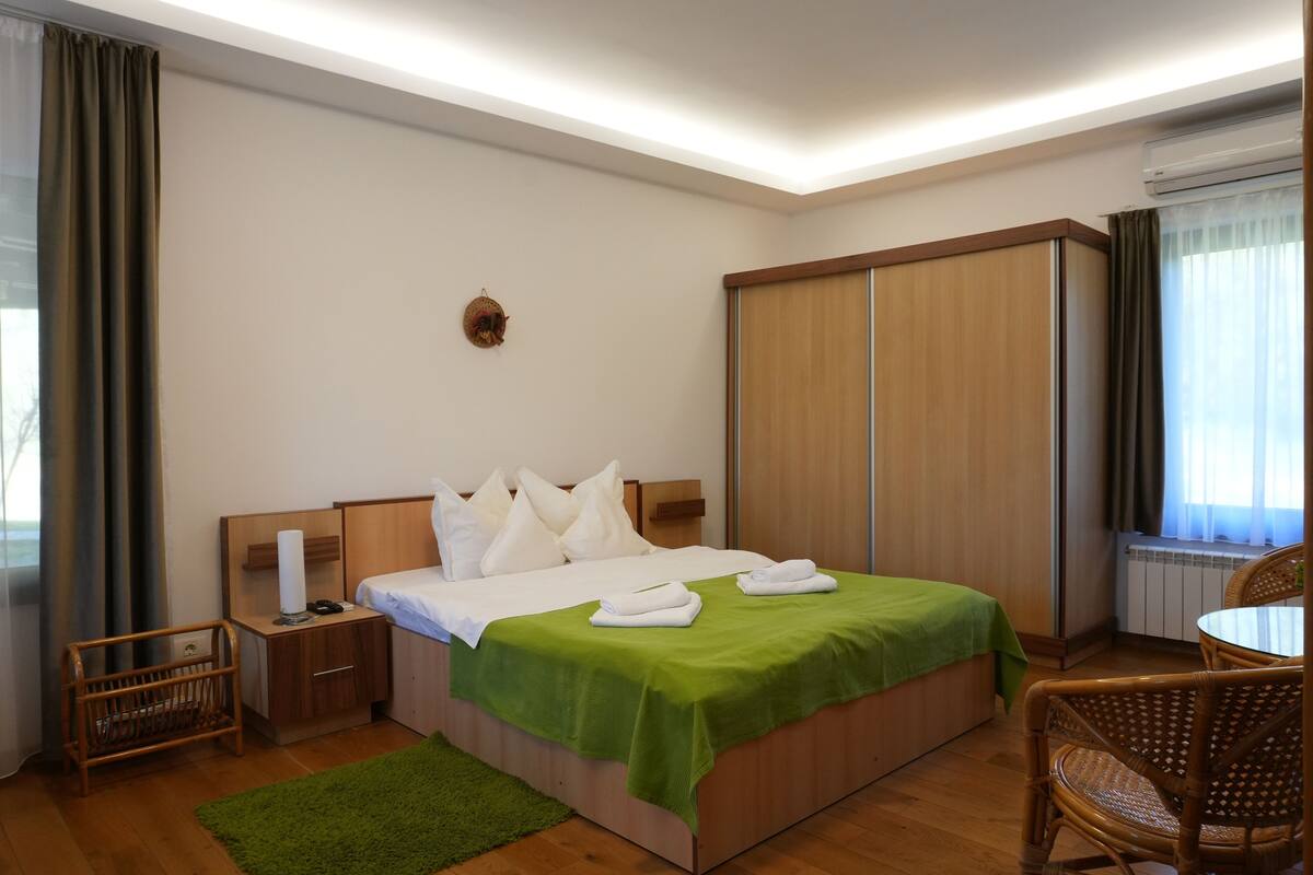 A hotel room with a bed, a wooden wardrobe, a wicker chair, and a small table.