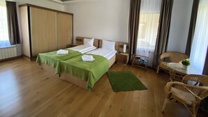 A hotel room with two beds, a wooden floor, a green rug, a small table with a chair, and a window with curtains. - Egreta By Hoxton (Murighiol)