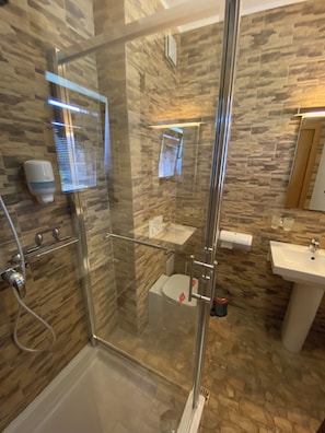 Un baño moderno con ducha envuelta en vidrio, un lavabo blanco y una pared con estampado de piedra.