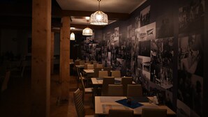 A dimly lit restaurant with wooden tables and chairs, hanging wicker lamps, and walls adorned with black-and-white photographs. - Egreta By Hoxton (Murighiol)