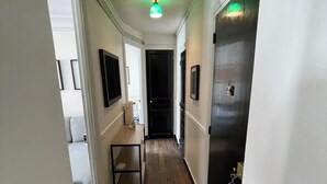 Un couloir avec un plancher en bois, des murs blancs et une porte noire au fond.