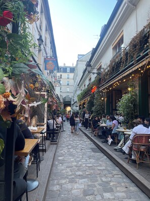 A narrow cobblestone street lined with outdoor seating areas and cafes, with people dining and walking. - Quartier Saint-germain-des-prés, au Cœur de Paris, Cathédrale Notre-dame (Paris)