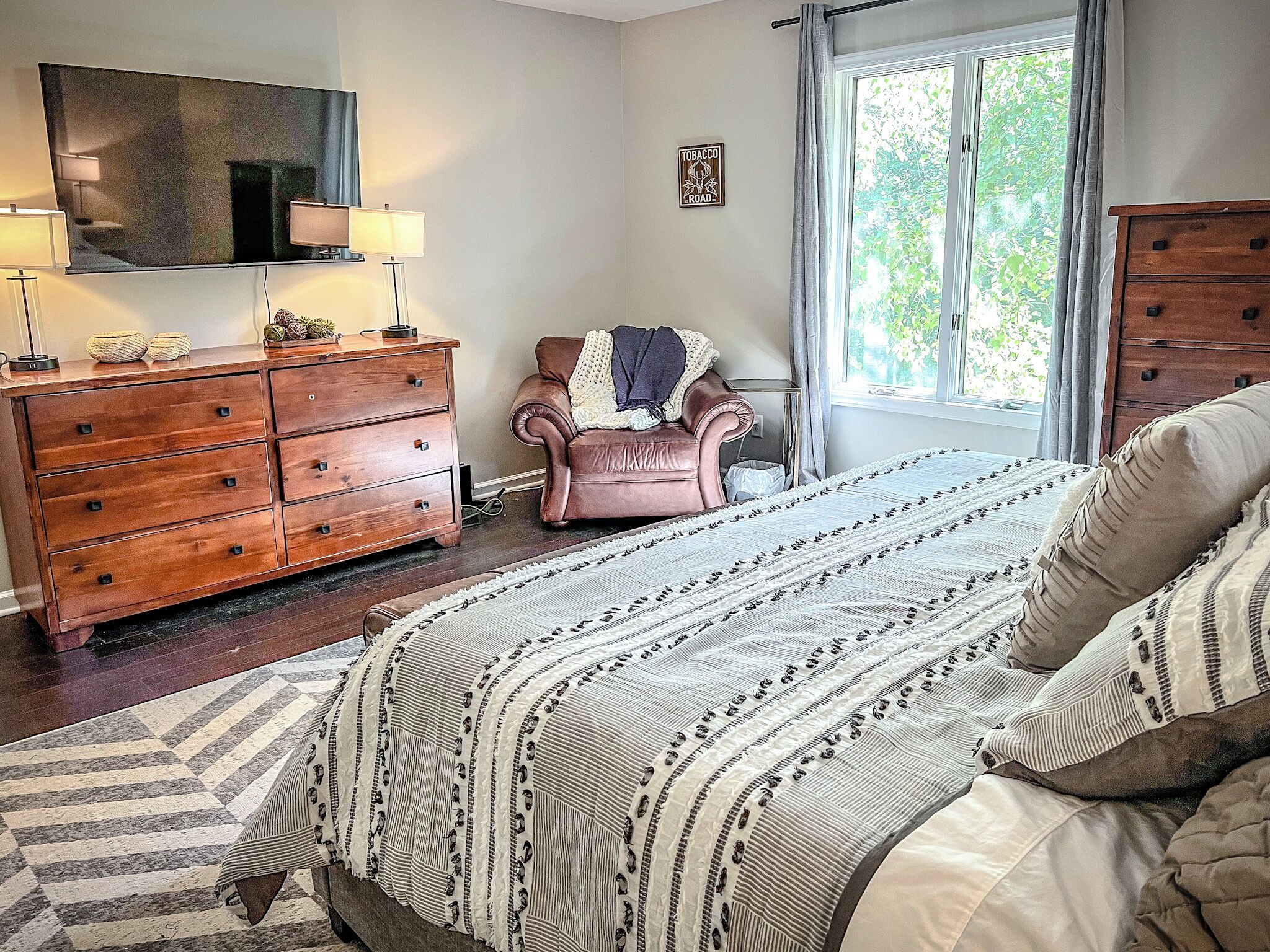 A bedroom with a bed, a dresser, a chair, a TV, and a window.