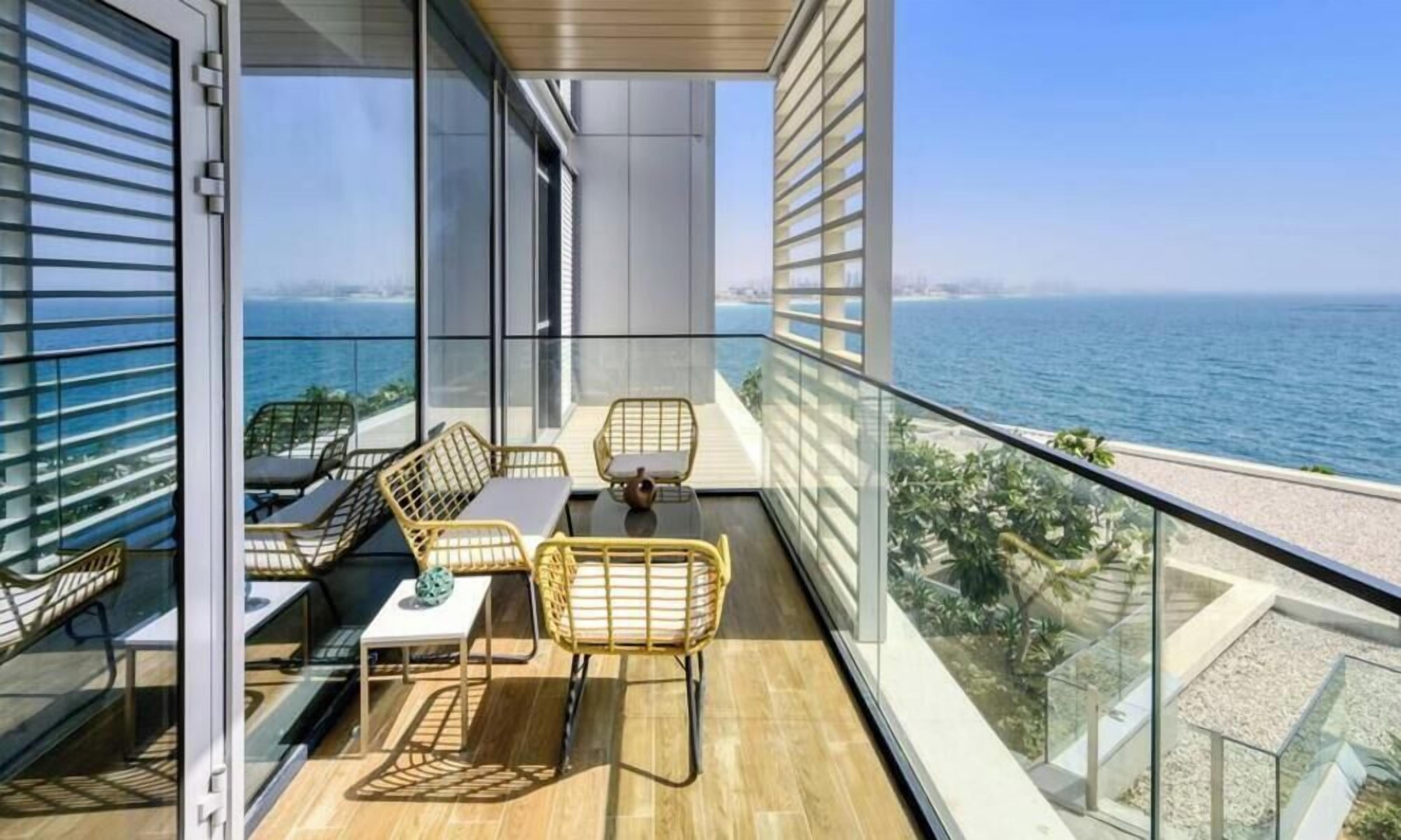 A balcony with a view of the sea, furnished with wicker chairs and a table.