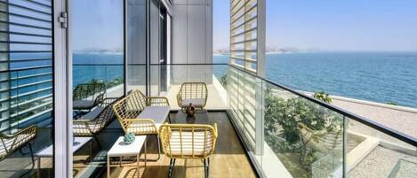 A balcony with a view of the sea, furnished with wicker chairs and a table.