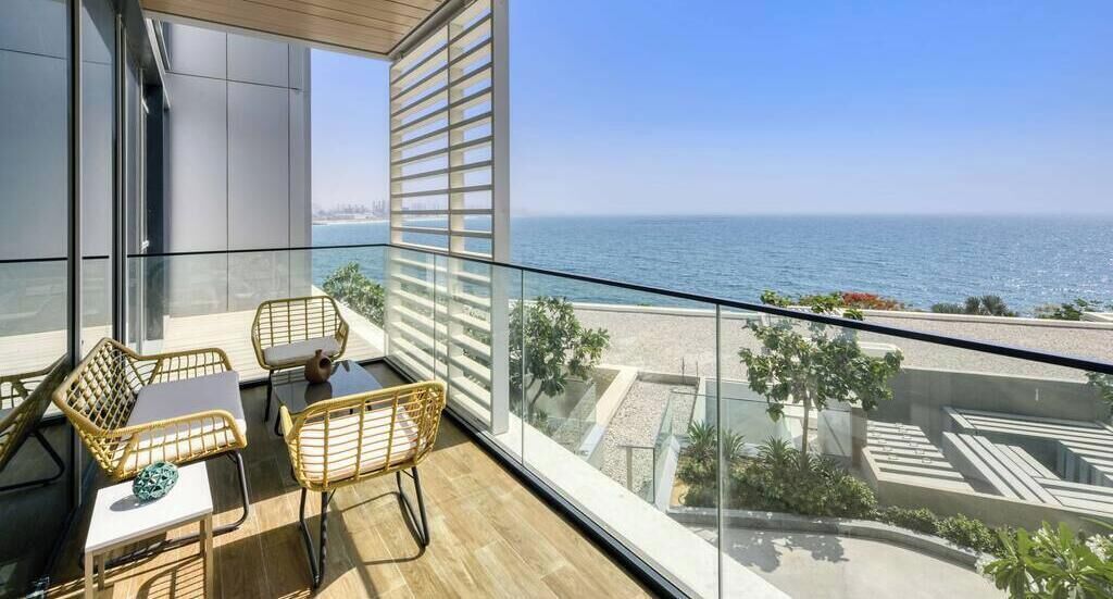 A balcony with a view of the sea, furnished with wicker chairs and a small table.