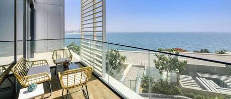 A balcony with a view of the sea, furnished with wicker chairs and a small table.