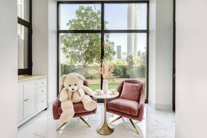 Une pièce avec une grande fenêtre, un ours en peluche blanc, une chaise rose et une petite table avec des tasses.