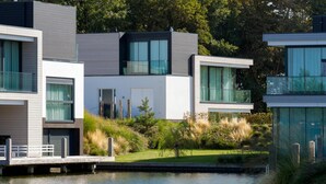 Ein modernes, mehrstöckiges Haus mit großen Fenstern, einem Steg und einer Rasenfläche.