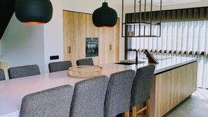 Eine moderne Küche mit einer zentralen Kochinsel, Holzschränken und einem großen Fenster mit Jalousien.