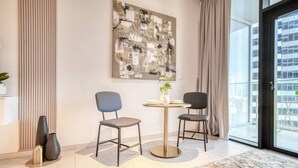 Un salon moderne avec un grand tableau abstrait, deux fauteuils, une petite table ronde et une vue dégagée sur l’extérieur grâce à une grande fenêtre.