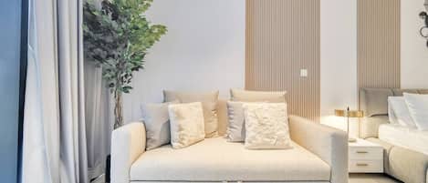 Une chambre moderne avec un canapé-lit, une table de chevet, une lampe et une plante en pot.