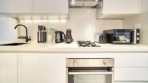 Une cuisine moderne avec des meubles blancs, un four encastré, une machine à café et un grille-pain.