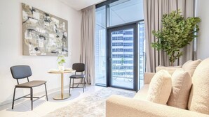 Un salon moderne comprenant un canapé, deux fauteuils, une petite table avec une plante et une grande fenêtre donnant sur des immeubles.