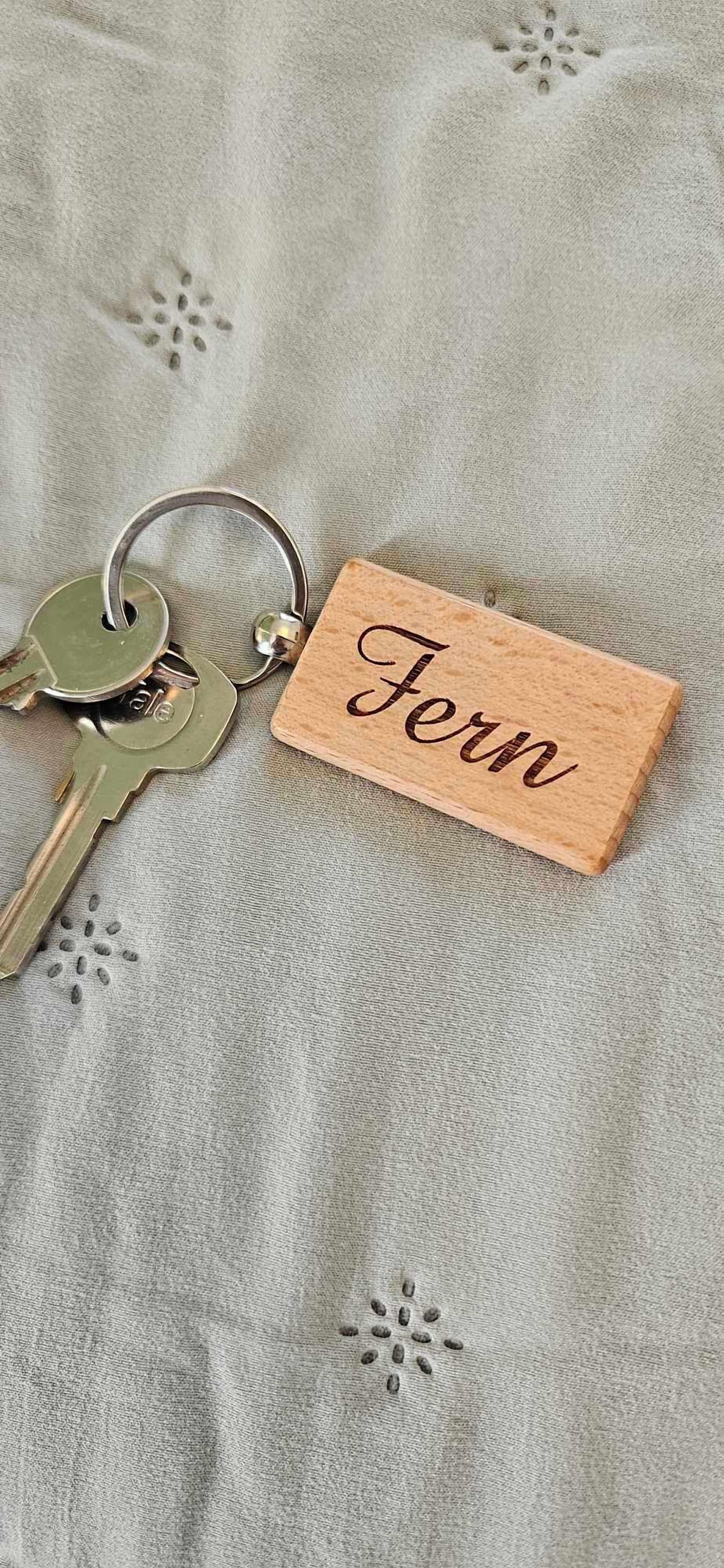 Een set sleutels met een houten labeltje met de naam 'Fern' op een gestructureerde stoffen achtergrond.