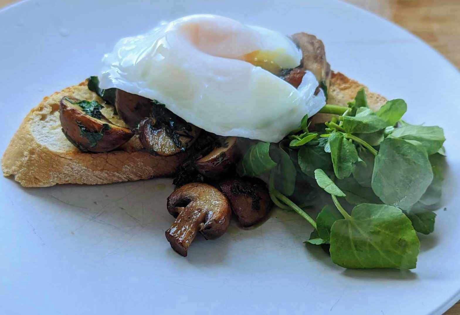 A plate with a poached egg, grilled mushrooms, spinach, and toast.