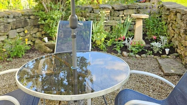 A glass table with a metal frame, surrounded by a stone wall and greenery, under a large umbrella. - Halmer Grange  (Whitby)