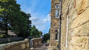 A stone building with a narrow pathway lined with potted plants and a stone wall. - Halmer Grange  (Whitby)