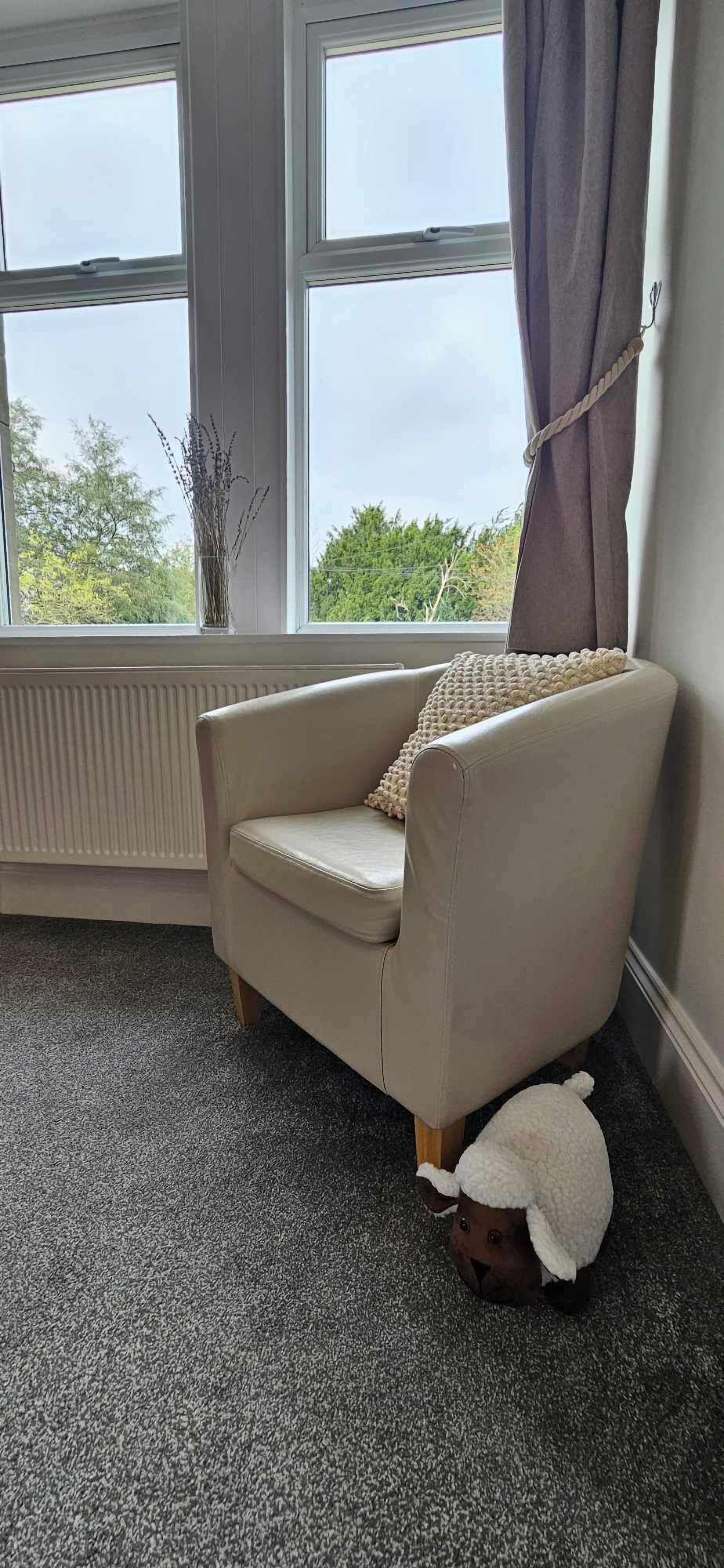 A corner room with a beige armchair, a small table, and a window with curtains.