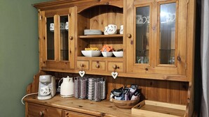 A wooden cabinet with glass doors containing plates, mugs, and a bowl. Below, there are coffee-making items and a basket of snacks. - Halmer Grange  (Whitby)
