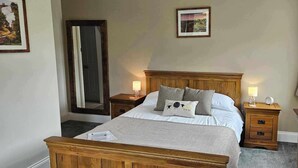 A neatly arranged bedroom with a wooden bed, two bedside tables, a nightstand, a mirror, and a framed picture on the wall. - Halmer Grange  (Whitby)