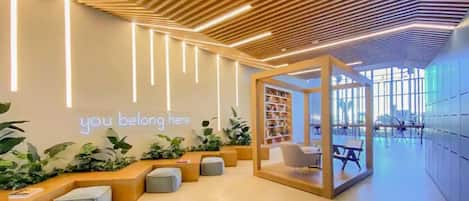 A modern reception area with a wooden ceiling, a neon sign, seating, a bookshelf, and a view through large windows.