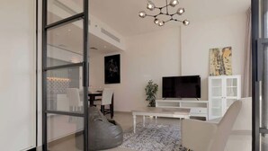 A modern living room with a glass door leading to a dining area, a flat-screen TV, a white cabinet, and a patterned rug.