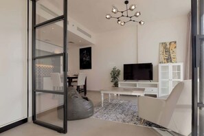 A modern living room with a glass door leading to a dining area, a flat-screen TV, a white cabinet, and a patterned rug.