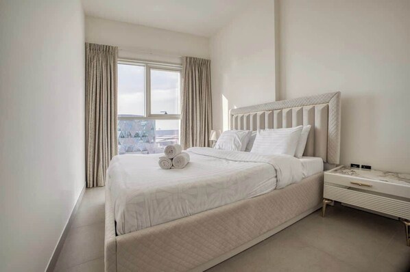 A hotel room with a large bed, a nightstand, and a window with curtains.