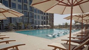 A swimming pool with lounge chairs and umbrellas, surrounded by a multi-story building.