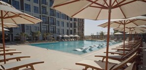 A swimming pool with lounge chairs and umbrellas, surrounded by a multi-story building.
