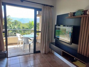 Relax in this stylish living room with a large flat-screen TV and sliding glass door leading to a balcony with a table and chairs.