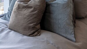 Een bed met veel kussens en een raam met gordijnen.