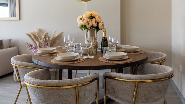 Een ronde eettafel met zes stoelen, een vaas met bloemen en een fles champagne.