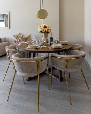 A round dining table with six chairs, a vase with flowers, and a bottle of champagne.