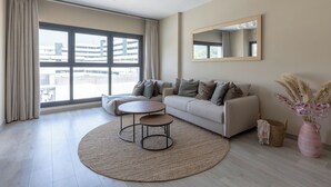 Een moderne woonkamer met een bank, een ronde salontafel en een groot raam met gordijnen.